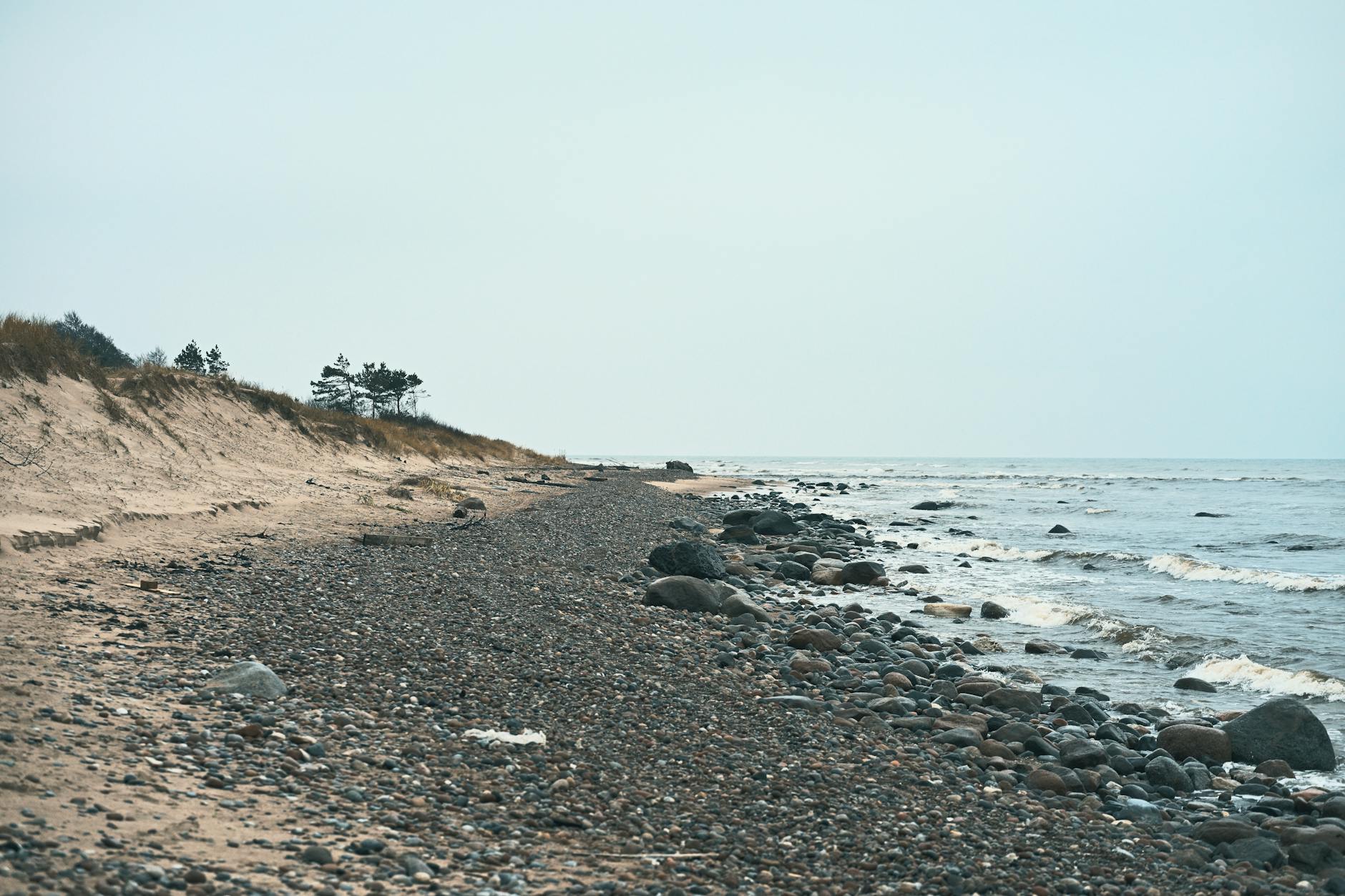 Gdzie uciec od tłumów latem? Ciche miejsca w Grzybowie, Dźwirzynie i pod Kołobrzegiem Spokojna, kamienista plaża nad morzem o zachodzie słońca