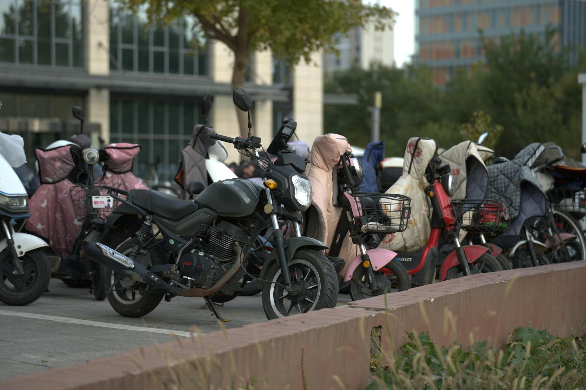 Zaparkowane hulajnogi i skutery pod pokrowcami przy miejskim chodniku