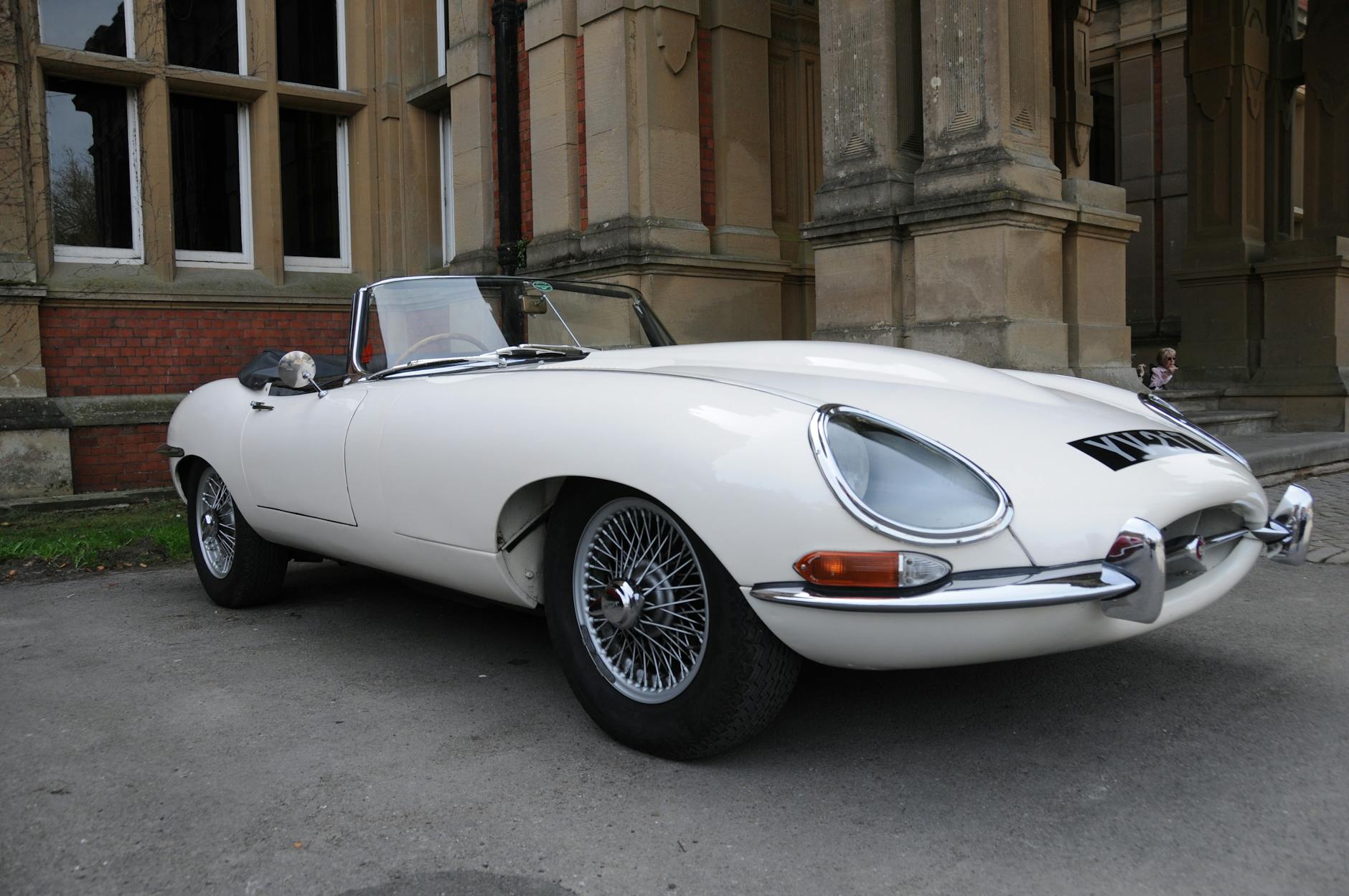Biały klasyczny Jaguar E-Type zaparkowany przed zabytkowym budynkiem