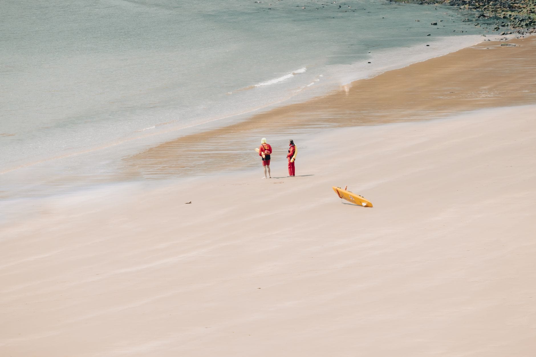 Dwóch ratowników na piaszczystej plaży nad morzem obok deski ratunkowej