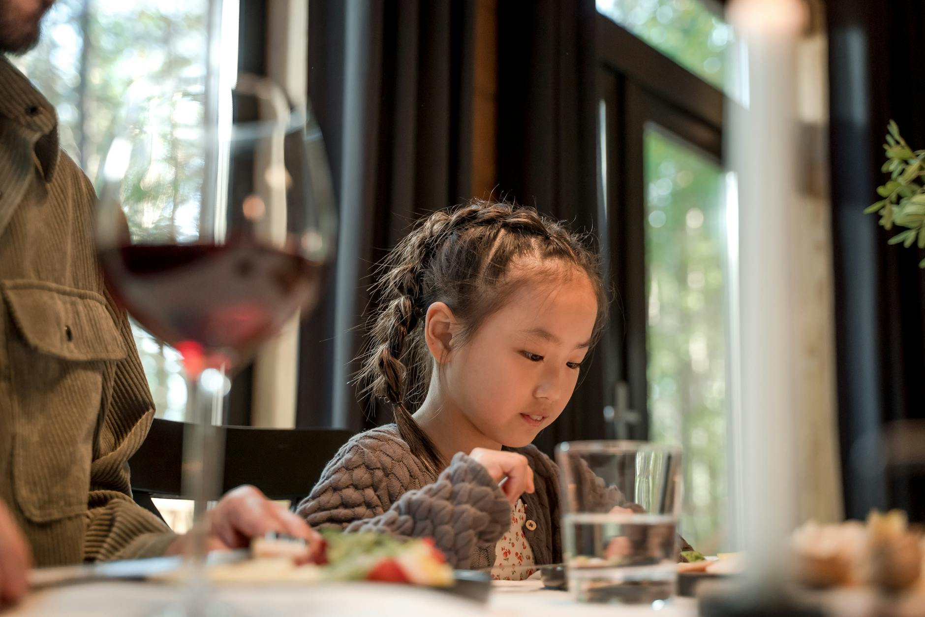Dziewczynka z warkoczykami je posiłek przy restauracyjnym stoliku