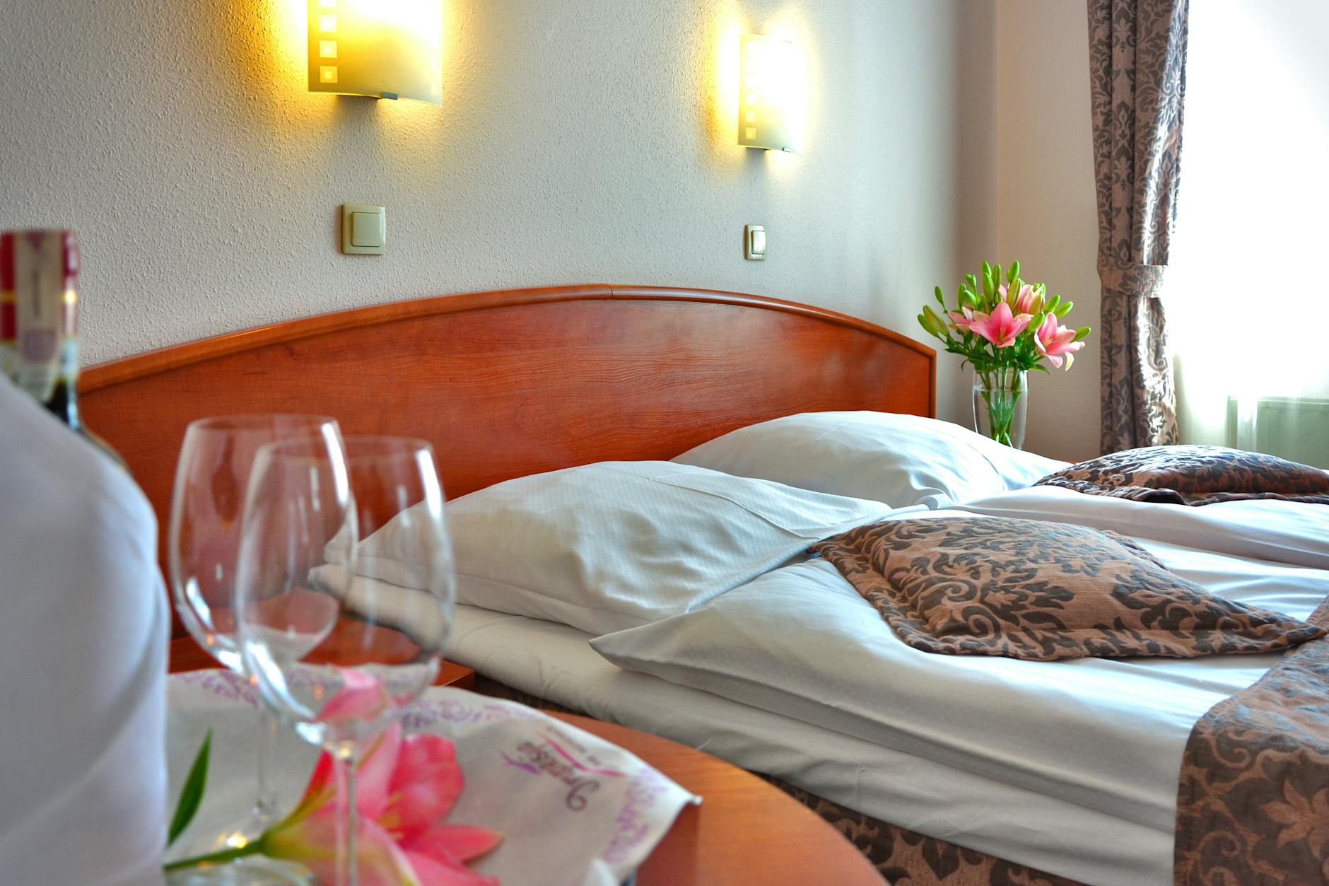 Elegancki pokój hotelowy z łóżkiem, kieliszkami wina i kwiatami