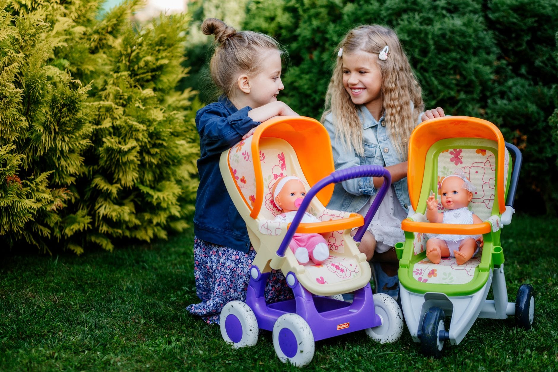 Dwie dziewczynki bawią się lalkami i wózkami w ogrodzie